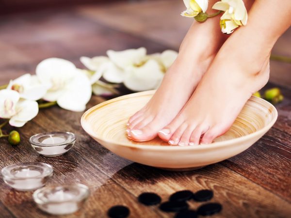 Closeup photo of a female feet at spa salon on pedicure procedure. Female legs in water decoration the flowers.